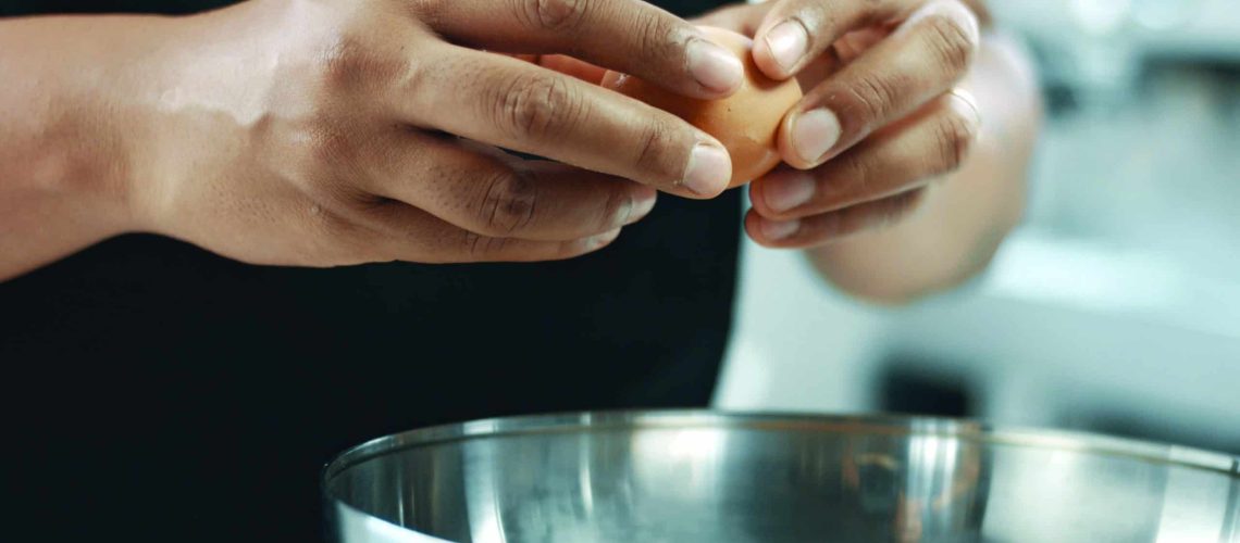 mixed race baker makes a cake. smash eggs